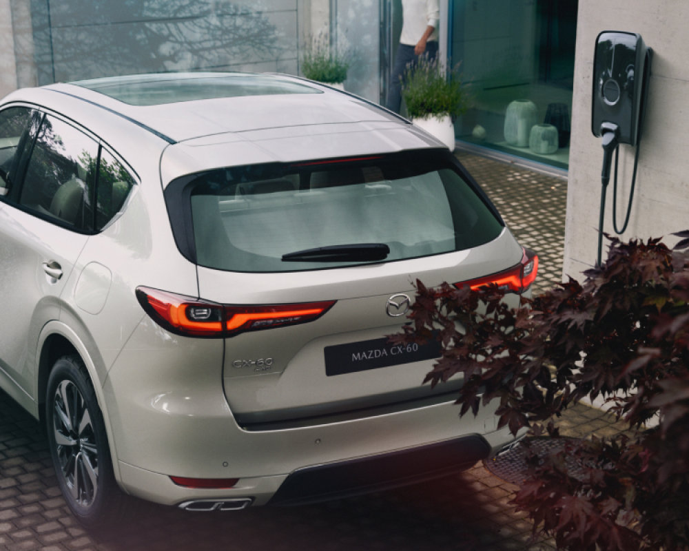 A Mazda CX 60 plug in hybrid parked in front of a house, showcasing its sleek design with the assistance of Mazda Finance.